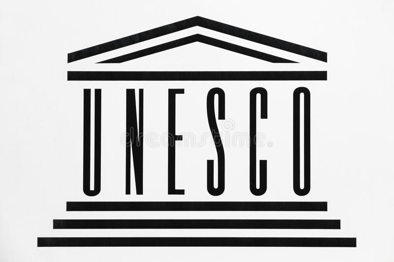 Logo przedstawia napis wielkimi literami: UNESCO. pod napisem znajdują się trzy poziome linie, a nad nim trójkąt w kształcie dachu.