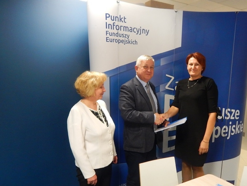 Na zdjęciu na biało-niebieskim tle napis: Punkt informacyjny funduszy europejskich. Przed tłem stoją trzy osoby: dwie kobiety, pomiędzy nimi mężczyzna - Jerzy Sirak.