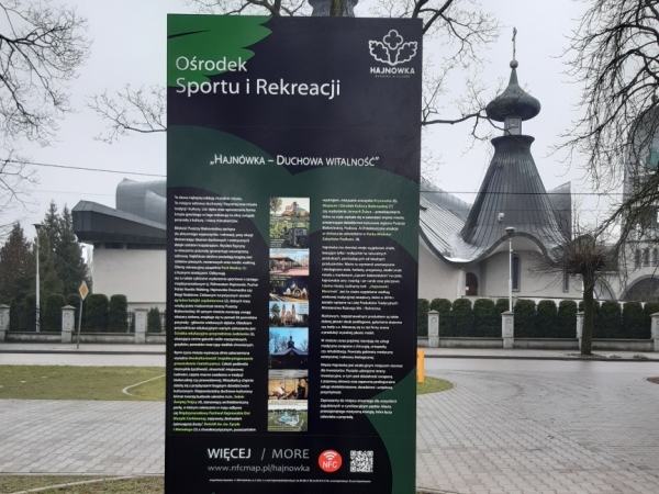 tablica turystyczna ustawiona na placu Ośrodka Sportu i Rekreacji w Hajnówce, na tablicy widoczna jest mapa, w tle Sobór św. Trójcy.