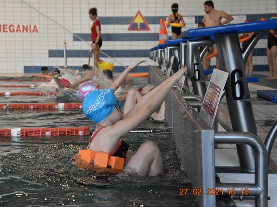 Zdjęcie przedstawia startujących zawodników w konkurcencji pływackiej. Na pierwszym planie dziecko w niebieskum czepku.