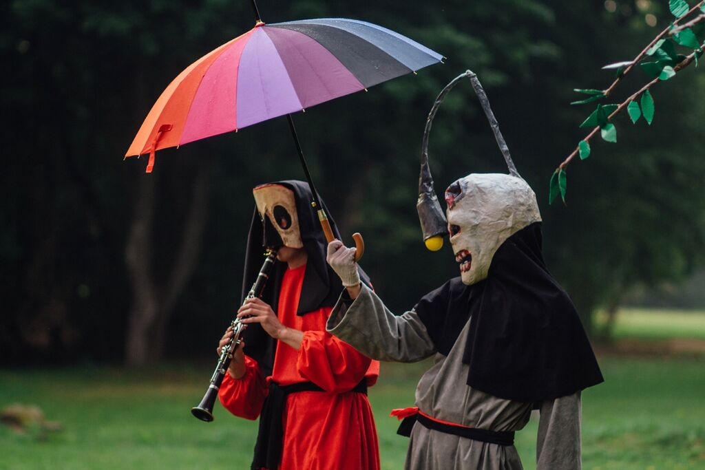 Jedna osoba gra na flecie, druga trzyma kolorowy parasol