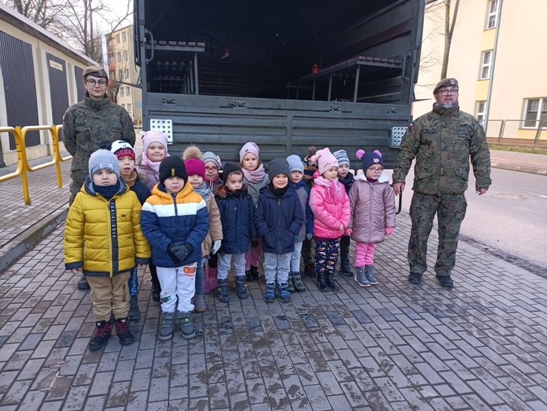 Dyrekcja przedszkola wraz z dziećmi i przedstawicielami służb mundurowych stoją przed budynkiem Przedszkola nr 5