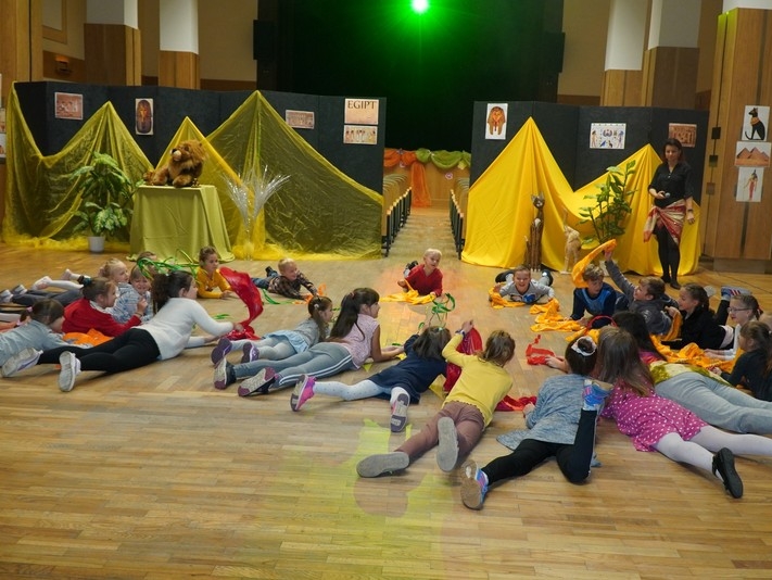 Dzieci leżące na podłodze za nimi piramidy z żółtego materiału