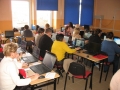 Uczestnicy szkolenia w trakcie spotkania, usadzeni są za szkolnymi ławkami, przed sobą na stolikach mają laptopy