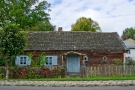zdjęcie przedstawia małą drewnianą wiejską chatę z niebieskimi oknami i drzwiami wejściowymi