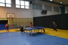 sala gimnastyczna, dwa stoły tenisowe, rzy których ustawieni sa zawodnicy