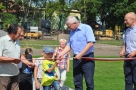 Na zdjęciu burmistrz Jerzy Sirak daje małemu chłopcu nożyczki, aby ten przeciął szarfę.