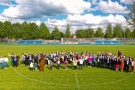 grupa mieszkańców miasta Hajnówka ok. 80 osób, ustawiona na zielonej murawie stadionu miejskiego; zdjęcie zrobione z drona