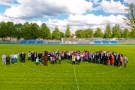 grupa mieszkańców miasta Hajnówka ok. 80 osób, ustawiona na zielonej murawie stadionu miejskiego; zdjęcie zrobione z drona