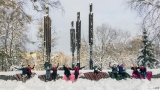 Grupa pań siedzi na kapach  W parku miejskim w ziomowej scenerii. W tle widać rzeźby "Niezłomnych"