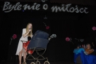 spiewajaca do mikrofonu dziewczyna pochyla się nad dziecięcym wózkiem. Nad nią widnieje napis: "Byle nie o miłości" 