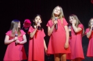 Grupa śpiewających dziewcząt w czerwonych sukienkach.