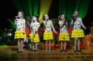 Pięć dziewczynek stoi na scenie, wszystkie ubrane w żółte spódnice i białe bluzki.