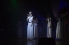 Na scenie stoją dziewczyny ubrane w jednakowe białe sukienki