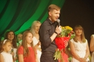 Mężczyzna trzymający bukiet kwiatów, za nim stoją wokalistki Studia Piosenki HDK