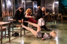 jedna ze scen spektaklu: jedna kobiekra leży na podłodze jej nogi trztma siędzący na stoliku mężczyna