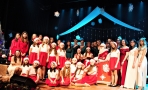 duża grupa wykonawców stoi na scenie. Wszyscy ubrani w czerwono białe stroje świąteczne