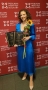Na zdjęciu widoczna jest kobieta w niebieskiej sukience. W dłoni trzyma kwiatka oraz dwa dyplomy.