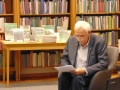 mężczyzna siedzi na fotelu, w tle widać ekspozycję jego książek