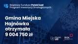 granatowy plakat informujący o otrzymanym przez gminę dofinansowaniu; zawiera wartość otrzymanych środków oraz nazwę programu Rządowy Fundusz Polski Ład: Program Inwestycji Strategicznych