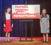 dwie dziewczynki stoją przy planszy z tytułem festiwalu