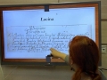 Prowadząca pokazuje planszę z tekstem w łacinie