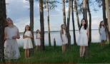 dziewczynki w białysch sukienkach stoją wśród drzew. W tle widać zalew.