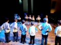 Dzieci tańczące na scenie stoją na przeciwko siebie i trzyają się pod boku