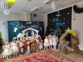 grupa małych dzieci ybranych jak aniołki stoi przy szopce