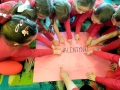 Zdjęcie przedstawia grupę dzieci z wyciągniętymi rękami wskazującymi napis „Walentynki”.