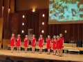 Dziewczęta w czerwonych sukienkach stoją na scenie. ztyłu wyświetlane są stare zdjęcia.