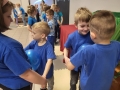 Dzieci stoją w parach odwrócone do siebie twarzami, pomiędzy soba trzymają niebieskie balony.