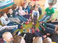 Dzieci z nauczycielką siedzą na zielonym dywanie.