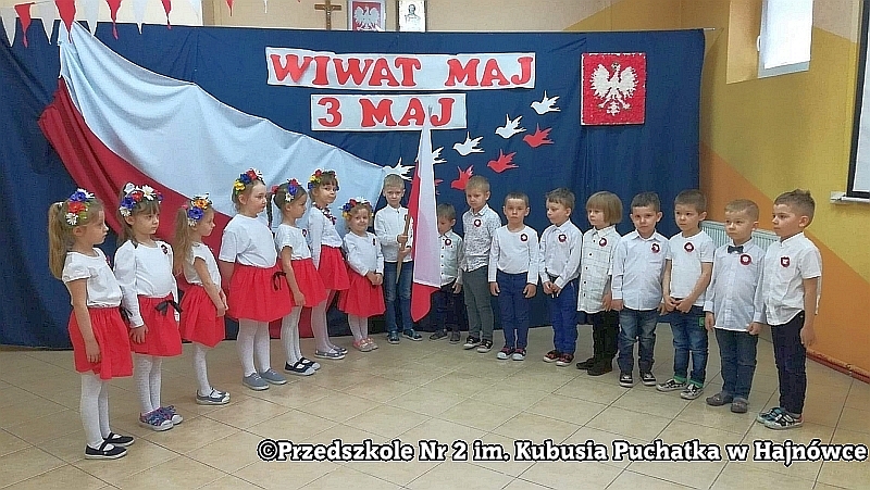 Dzieci ustawione są w półkolu w tle patriotycznej dekoracji