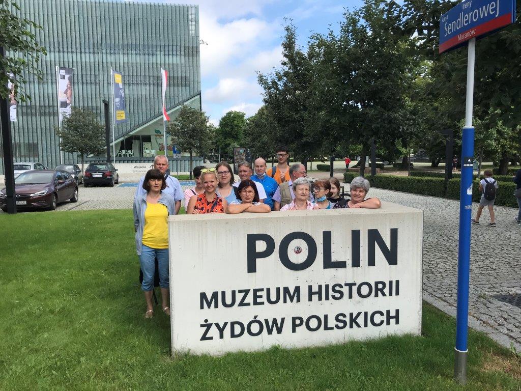 Grupa wycieczkowiczów pozuje do zdjęcia pamiątkowego przy pomniku Muzeum POLIN