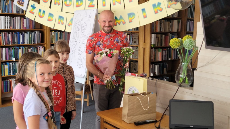 Tomasz Samojlik trzyma kwiaty, po lewej stoi grupa dzieci.