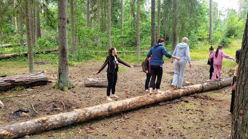dzieci i dorosli przechodzą bosą po leżacym drzewie