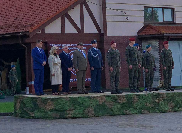 dziesięć osób stoi na podwyższeniu. Siedem z nich jest w mundurach.