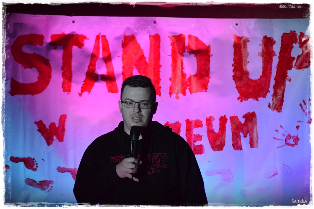 mężczyzna z mikrofonem. W tle widać podświetlony napis STAND UP 