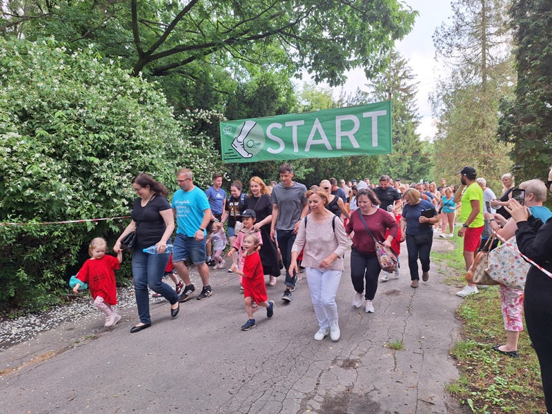 dzieci i opiekunowie biegną przez park miejski