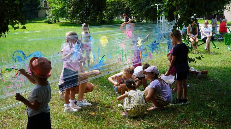 dzieci malują na folii rozciągniętej między drzewami