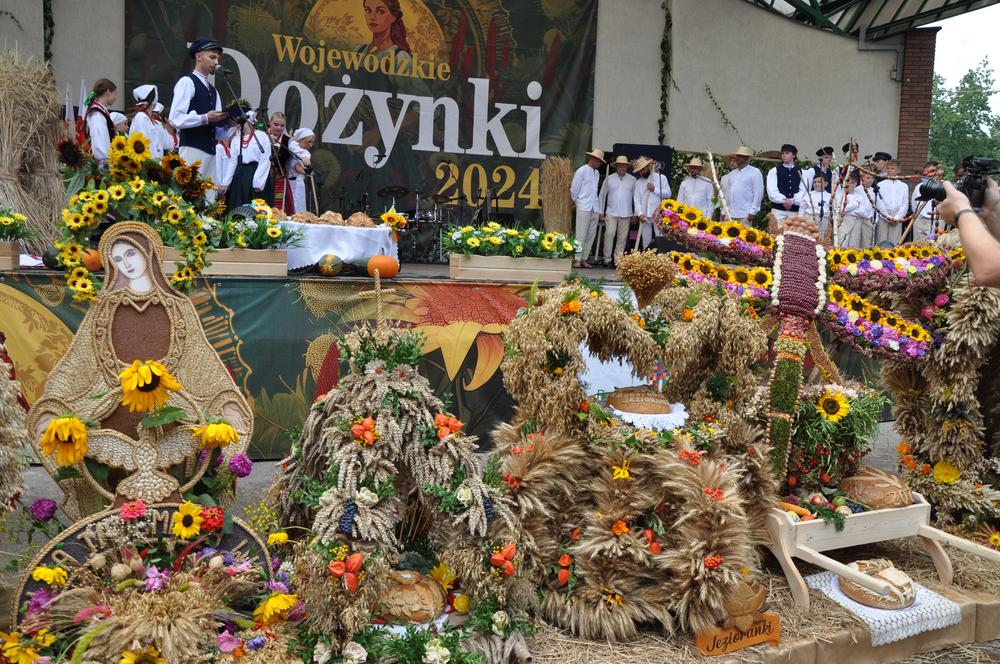 zespół występuje na scenie. Pod scena ustawione wieńce dożynkowe. 