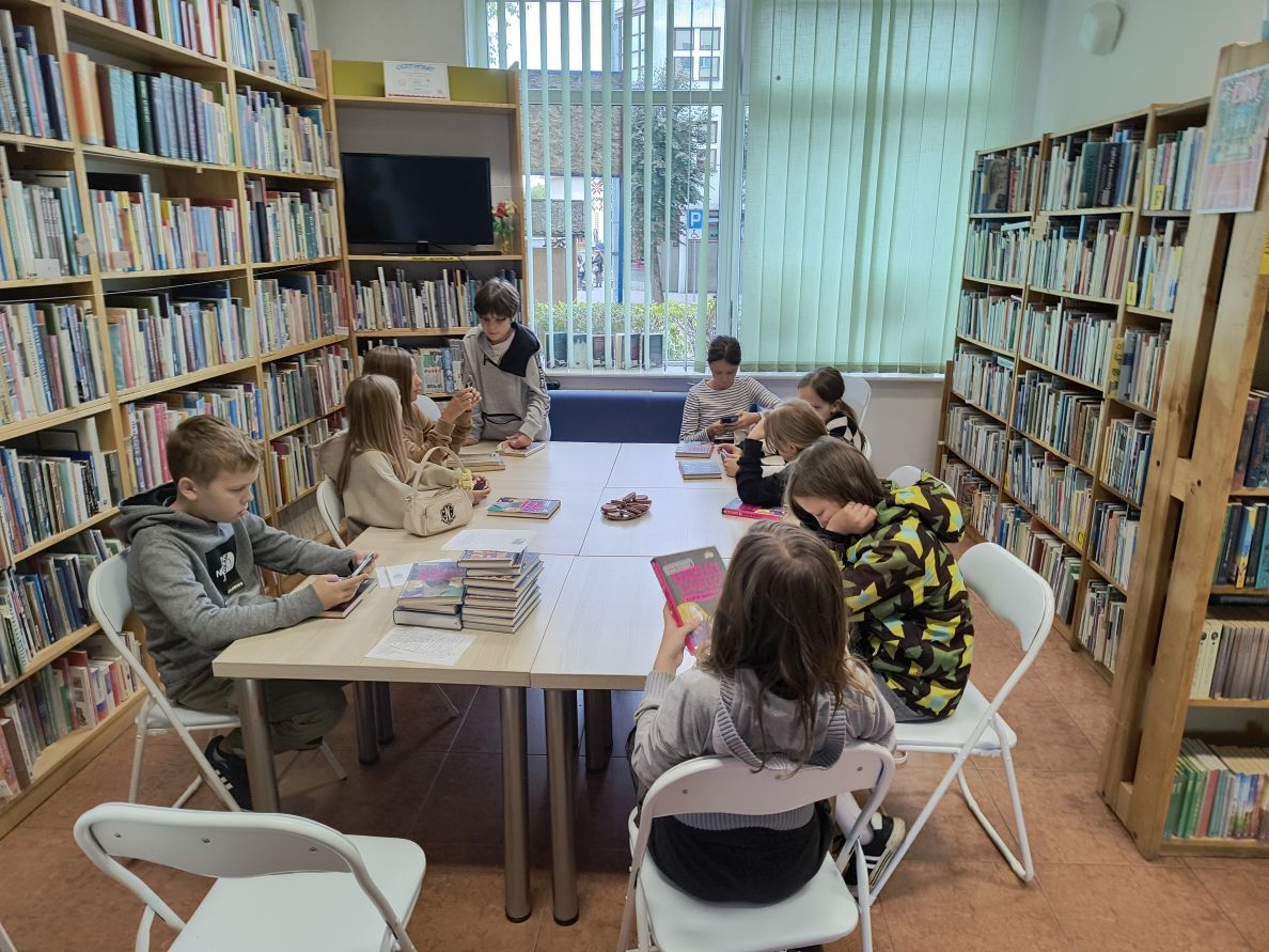 dzieci siedzące przy stole w bibliotece. Na stole leżą książki