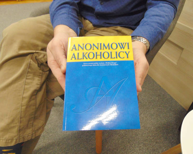 zbliżenie - mężczyzna prezentuje książkę o tytule "Anonimowi alkoholicy"