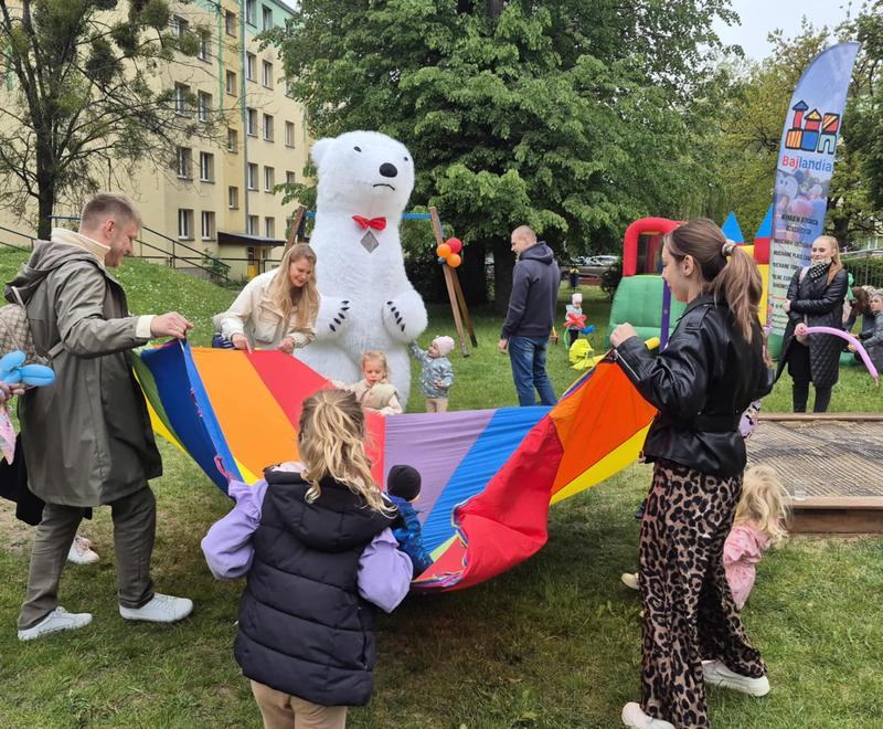 dzieci i rodzice podczas zabawy na pikniku. W tle widać maskotę dużego misia