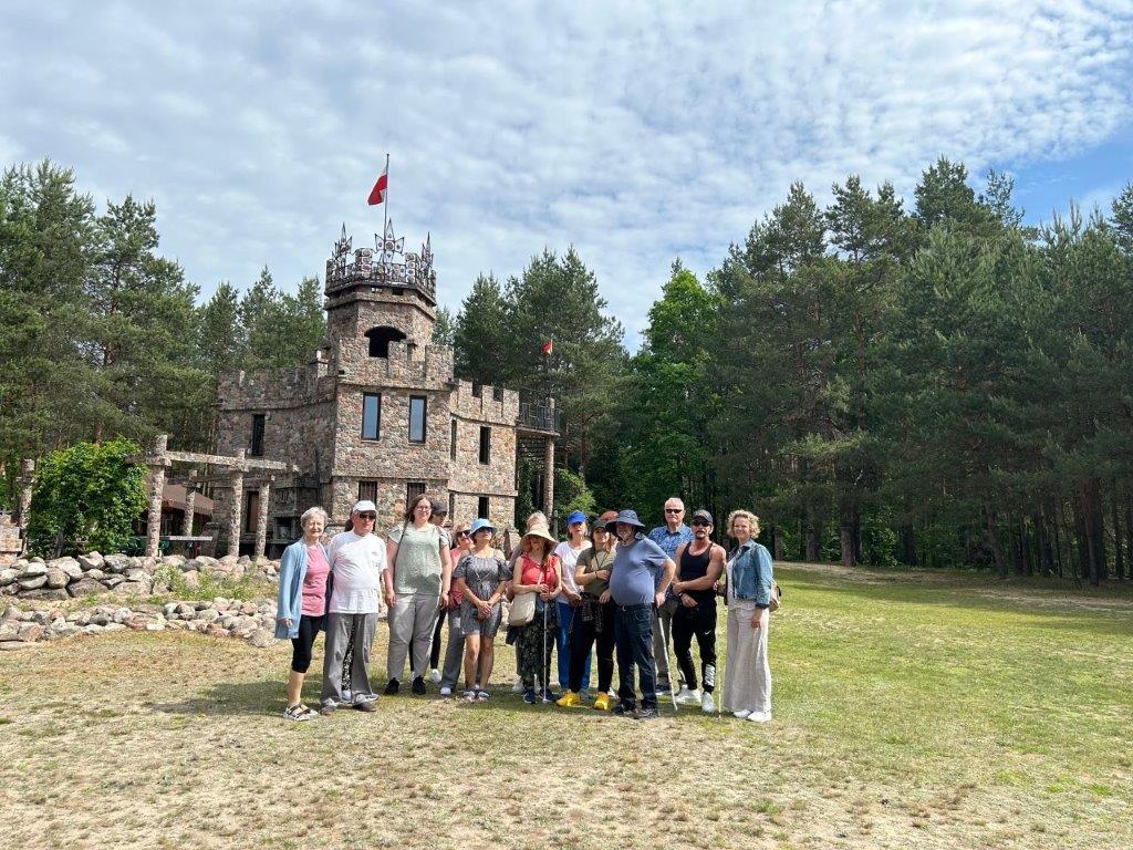 Gupa osób pozuje do zdjęcia przed Zamkiem Kasztelik