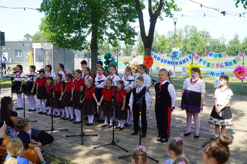grupa dzieci w strojach estradowych występuje w plenerze. W tle widać napis: Podsumowanie roku artystycznego.