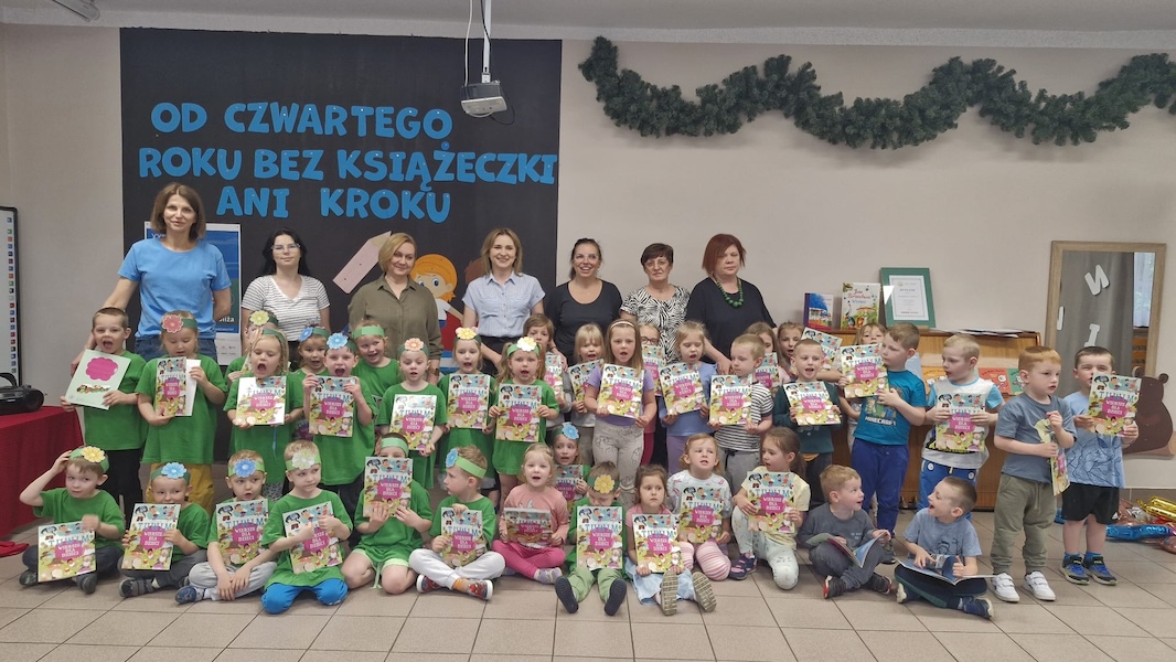 dzieci z dyplomami oraz opiekunki pozują do zdjecia W tle widać napis OD CZWARTEGO ROKU BEZ KSIĄŻECZEK ANI KROKU