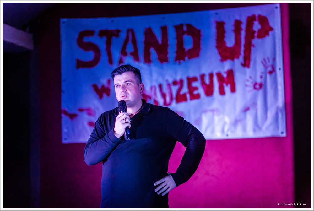 mężczyzna z mikrofonem. W tle napis STAND UP W MUZEUM