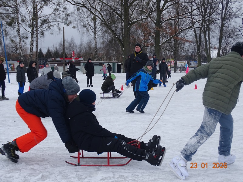 konkurencje na lodzie w tr&oacute;jkach. Jedno dziecko siedzi na sankach, inne dzieci ciągną i pchają sanki.